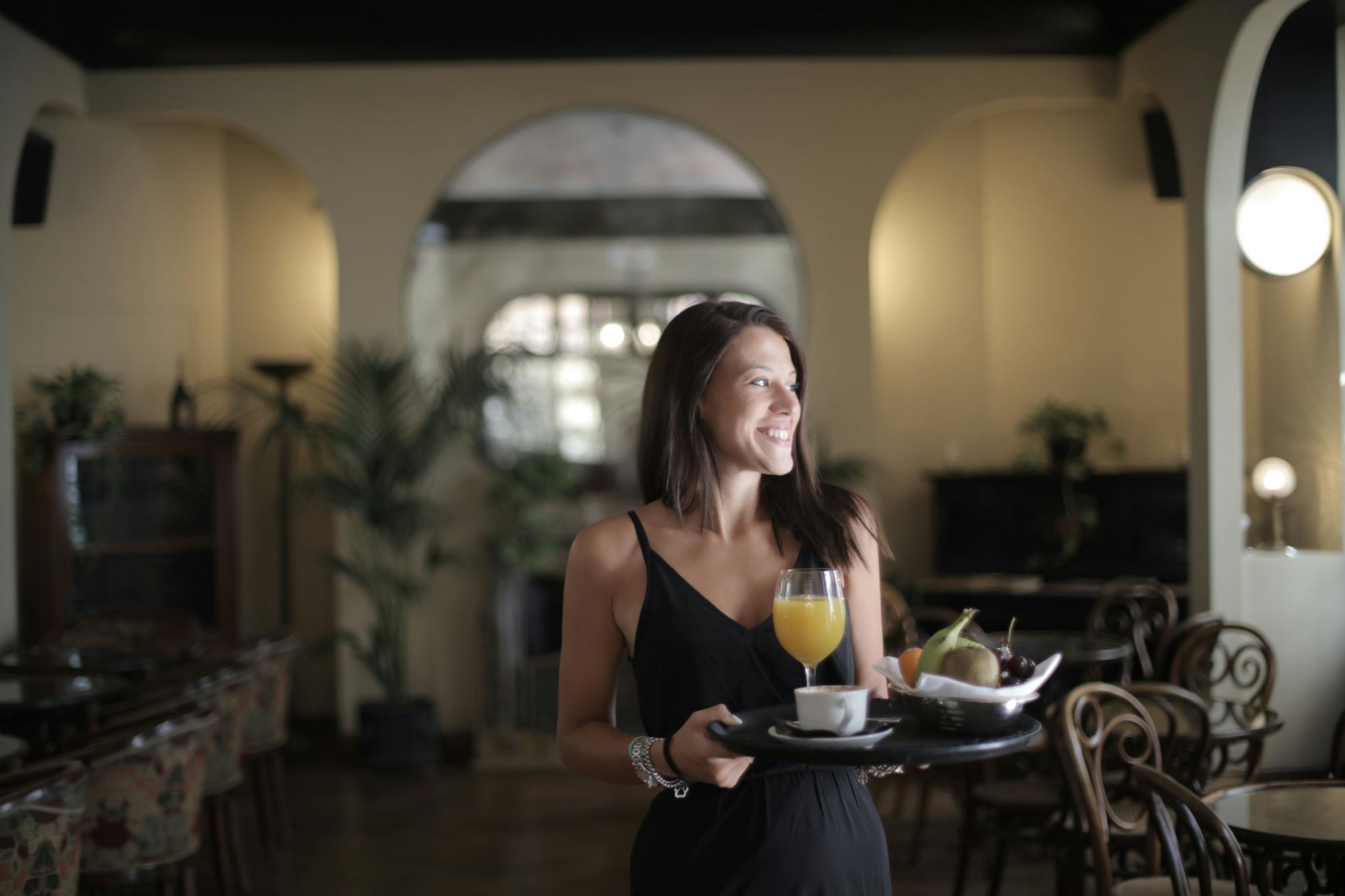 A cheerful woman serves breakfast with coffee and juice in a charming café setting.