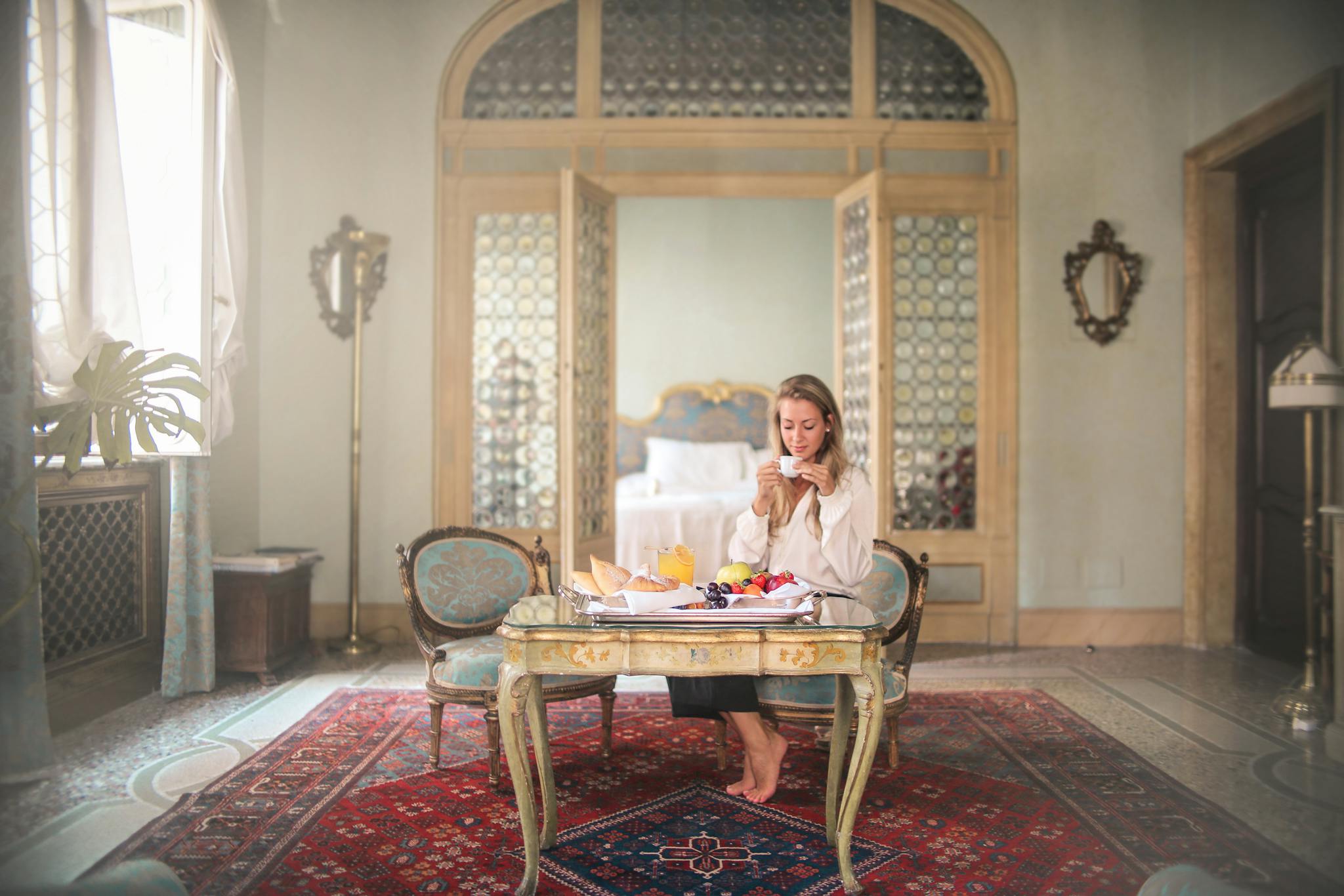 A woman relaxes with breakfast in a luxurious, classic-style hotel room with intricate details.