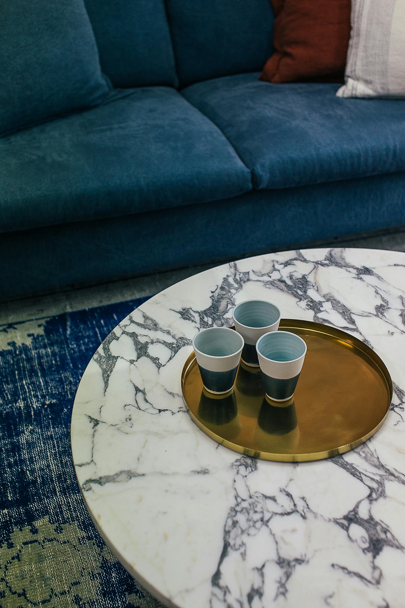 High angle of table served with cups of drink on tray near couch with pillows on carpet in house