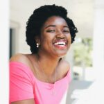 Portrait of a joyful woman in a pink top, smiling brightly outdoors on a sunny day.
