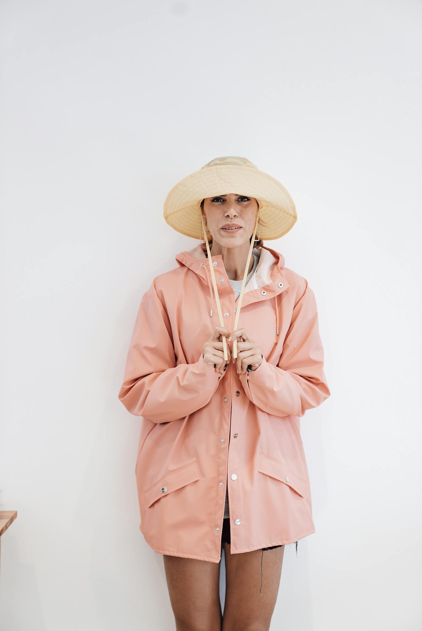 Stylish woman in a pink jacket and straw hat posing against a white background.